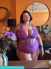 Woman wearing a purple lingerie set in a room with orange walls and decorative elements.