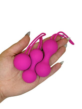 Hand holding three pink ball-shaped objects with strings against a white background
