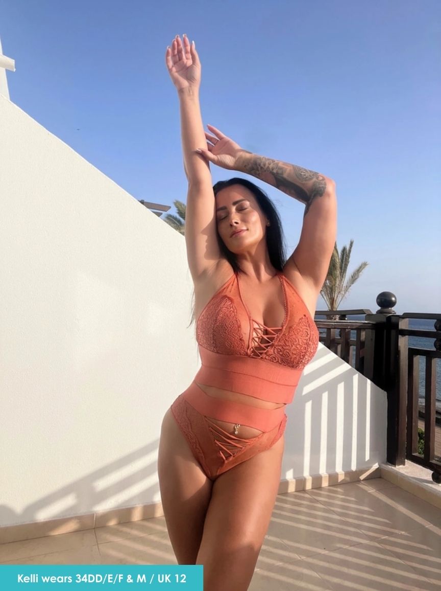 Woman in an orange bikini standing on a balcony with a clear blue sky.