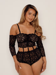 Woman wearing a black lace lingerie bodysuit against a plain background